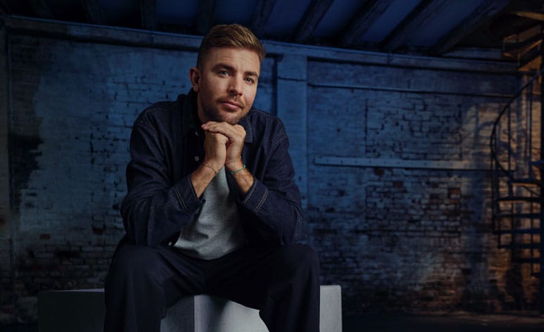 Fußballweltmeister Christoph Kramer sitzt auf einem Betonblock im blauen Interview-Raum und blickt in die Kamera.