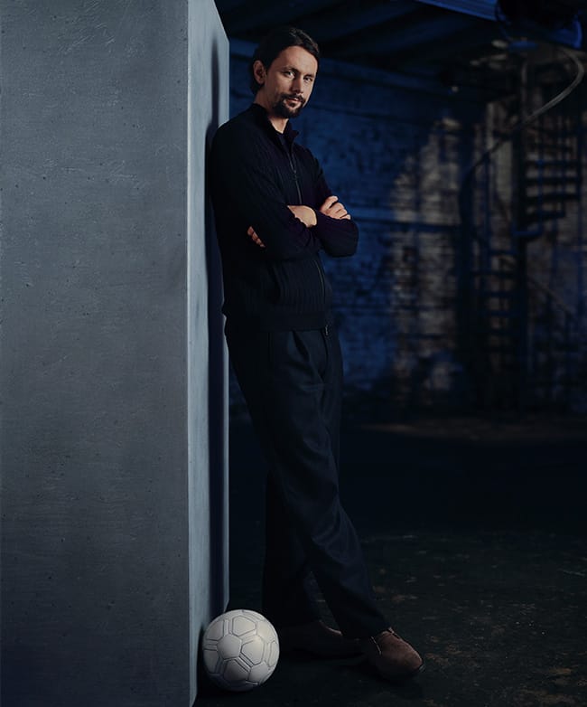 Neven Subotić lehnt mit verschränkten Armen an einem Betonblock, ein Fußball liegt zu seinen Füßen.