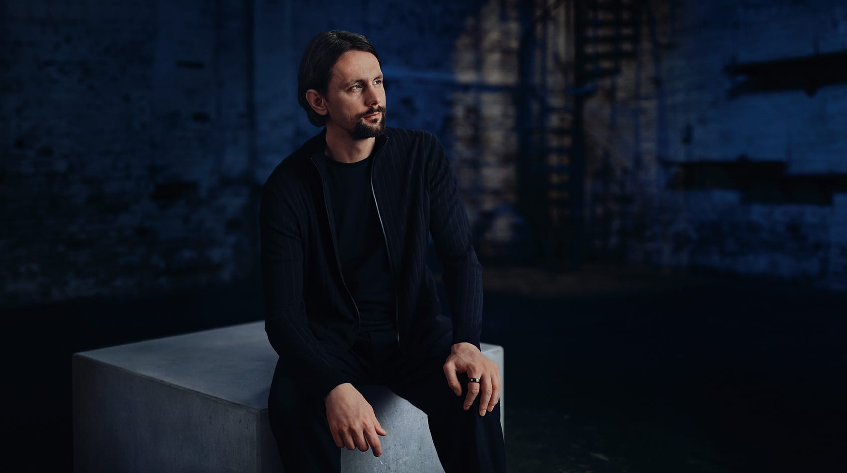 Neven Subotić sitzt nachdenklich auf Betonklotz vor blauer Backsteinwand. Er trägt ein dunkelblaues Outfit.