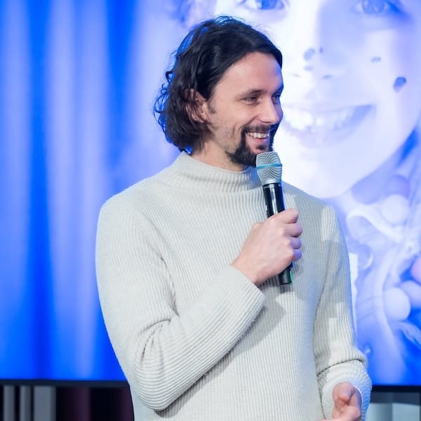 Neven Subotić spricht lächelnd in ein Mikro; im Hintergrund ein blaues unscharfes Kinderporträt.