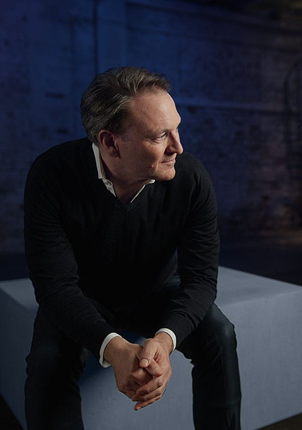 André Haagmann auf einem grauen Betonquader vor einer blauen Wand.