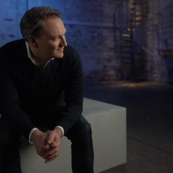 André Haagmann auf einem grauen Betonquader vor einer blauen Wand.