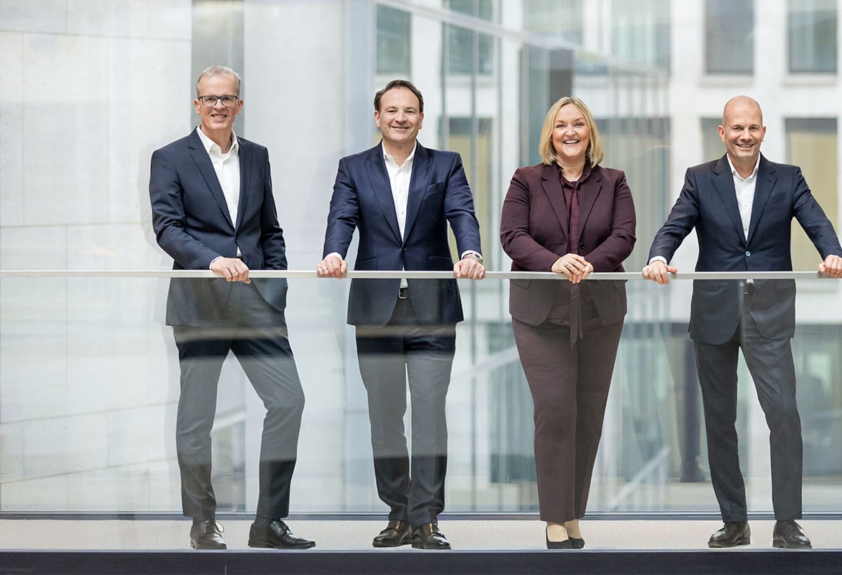Querformatiges Gruppenfoto des Vorstands von Union Investment in einem modernen Atrium mit Glasbrüstung.